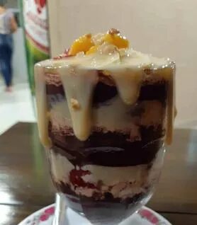 Copo de açaí em camadas com calda escorrendo, servido na mesa do salão